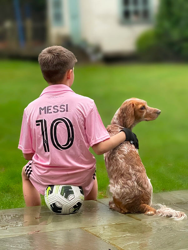 Portrait pris à l'iPhone 12 Pro d'un garçon en maillot Messi et de son chien, utilisant le mode Portrait avec un flou bokeh progressif et un excellent détourage du sujet.