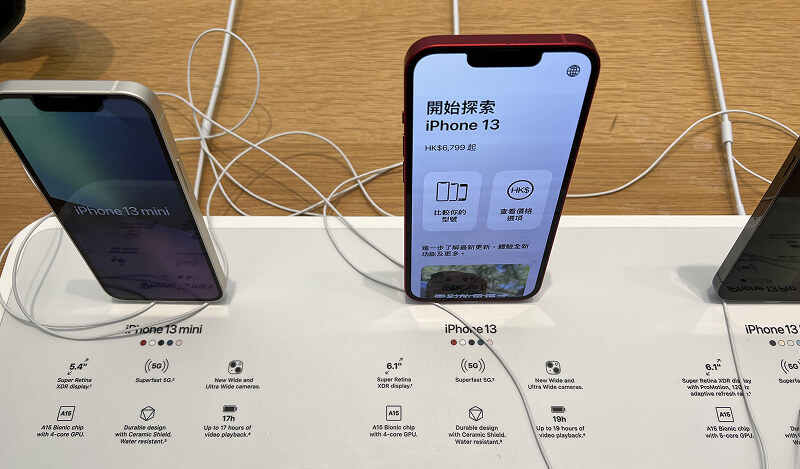 iPhone 13 et 13 mini exposés sur un présentoir avec écran allumé.