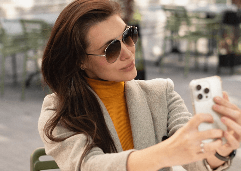 Femme prenant un selfie avec son iPhone 13 Pro en terrasse de café.