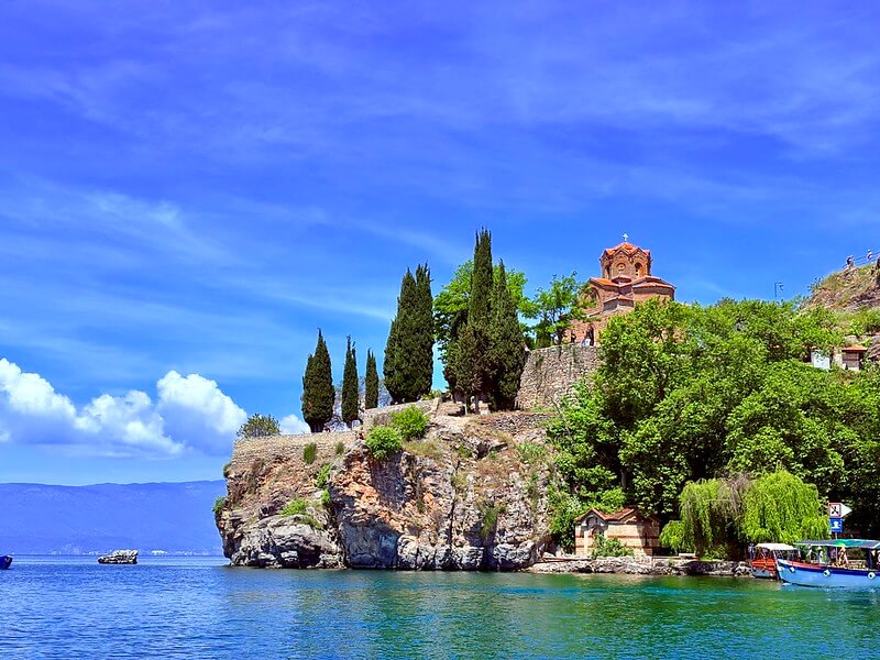 Rendu éclatant des paysages méditerranéens avec l'iPhone 16 : le château sur la falaise et la mer d'un bleu azur intense, capturés avec une saturation parfaite en plein jour.