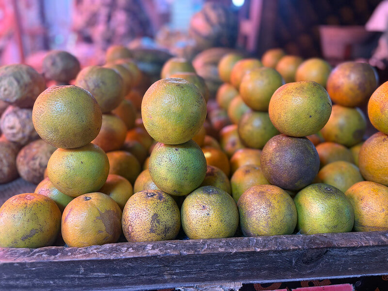 Photo en mode Portrait avec l'iPhone 16 : mise en valeur des fruits orange sur un marché avec un effet bokeh de qualité professionnelle, capturant la texture et les couleurs vives.